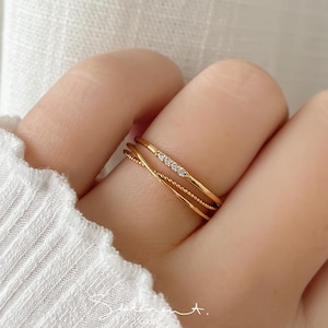 May include: A set of three gold rings with a delicate design. The middle ring features a row of small, clear stones.