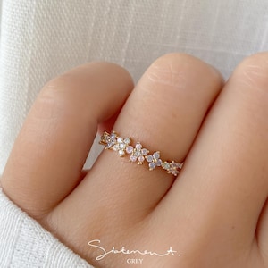 May include: A gold ring featuring a dainty design of small flowers adorned with clear and pink gemstones.