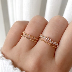 May include: Two gold rings with delicate designs. The top ring features a row of small diamonds, while the bottom ring has a more intricate design with larger diamonds in the shape of leaves.