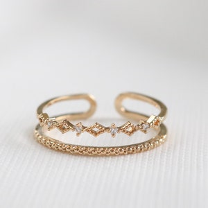 May include: A gold-toned adjustable ring featuring a delicate, textured band and a row of small, clear stones set in a geometric pattern.