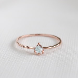 May include: A delicate rose gold ring with a single pear-shaped clear gemstone.