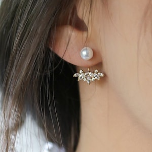 Op de afbeelding: Een paar gouden oorbellen met een parel en een cluster van heldere strass steentjes. De oorbellen zijn ontworpen om te worden gedragen met de parel aan de voorkant en de strass aan de achterkant.