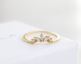 May include: A delicate gold ring with a crown of small, clear stones. The ring is on a white box with the text "Shakeman Jewelry" written in black.