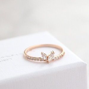Op de afbeelding: Een delicate ring van roségoud met een vlinderontwerp met drie marquisevormige stenen. De ring is bezet met kleinere ronde stenen langs de band.