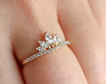 May include: A gold ring with a crown design featuring clear cubic zirconia stones.