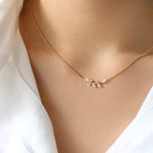 May include: A delicate gold necklace featuring a small, leaf-shaped pendant set with clear gemstones.