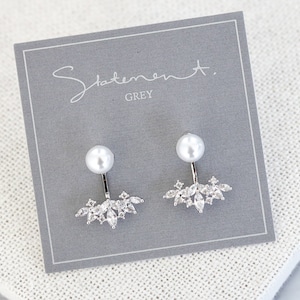 May include: Silver statement earrings featuring a pearl and a cluster of clear rhinestones. The earrings are displayed on a grey card with the text "Statement. GREY".