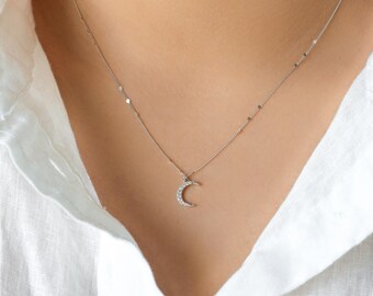 May include: A silver chain necklace with a crescent moon pendant encrusted with small clear stones.