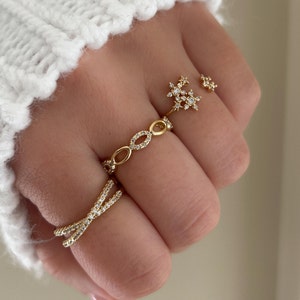 Peut inclure: Un ensemble de quatre bagues en or avec des pierres en zircone cubique transparentes. Les bagues présentent différents motifs, dont une chaîne délicate, une bande simple et un motif en forme d'étoile.