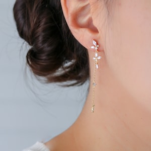 May include: Gold dangle earrings with a cluster of clear cubic zirconia stones at the top and a delicate chain extending down to a crescent moon charm.