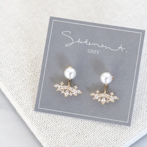 May include: A pair of gold earrings with a pearl and a cluster of clear rhinestones. The earrings are on a grey card with the text "Statement. GREY".