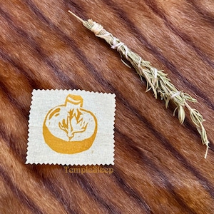 May include: A gold-colored stamp of a fig on a beige fabric square with the text "TempleSleep" printed below the fig.