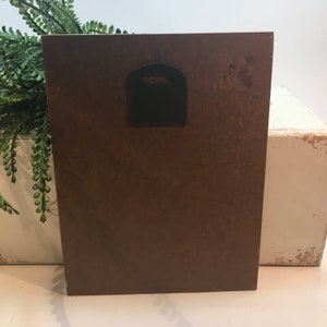 以下が含まれることがあります： 背面に黒い金属製のハンガーが付いた、茶色の木製の写真フレームの背面です。