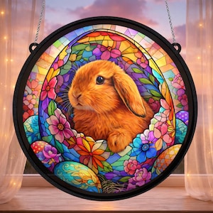 May include: Circular stained glass window art depicting a fluffy orange rabbit surrounded by colourful flowers and Easter eggs. The artwork is set in a black frame and hangs from a chain, ideal for Easter decorations.