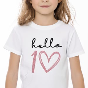 May include: White t-shirt with the text "hello 1" in black and a pink glitter heart.