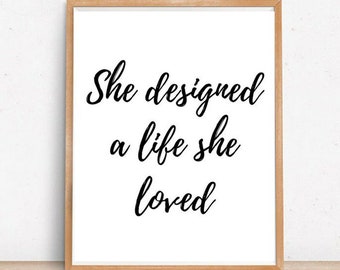 Puede incluir: Una impresión enmarcada con fondo blanco y texto negro que dice "She designed a life she loved."