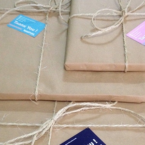 May include: Three packages wrapped in brown paper with twine and tied with a bow. Each package has a small card attached with the text "Thank You!" printed on it. The cards are in different colors: blue, pink, and blue.