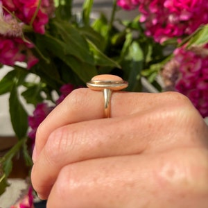 May include: A gold ring with a light pink oval gemstone set in a bezel setting.