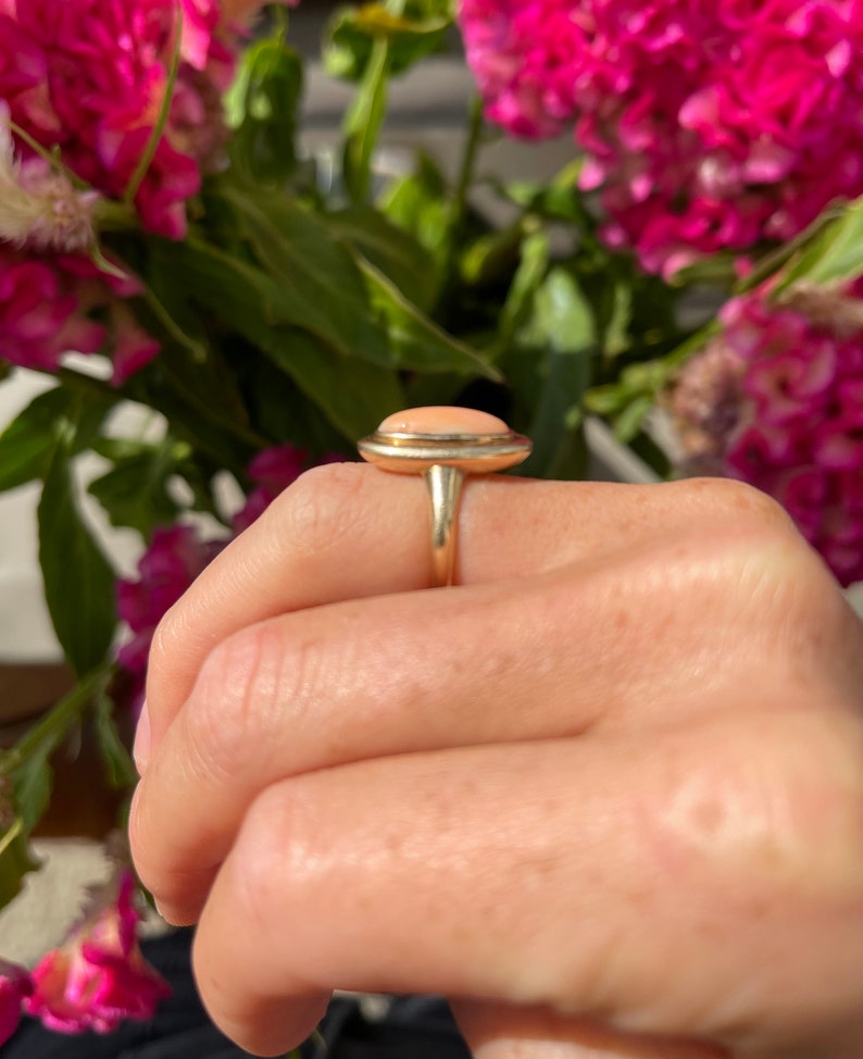 May include: A gold ring with a light pink oval gemstone set in a bezel setting.