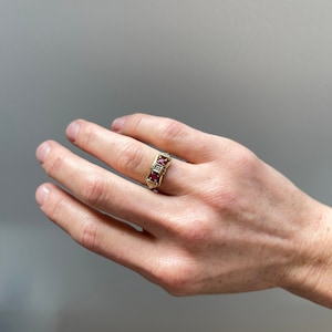 Puede incluir: Un anillo de oro con tres piedras preciosas rojas y un diamante. El anillo está engastado en un diseño delicado e intrincado.