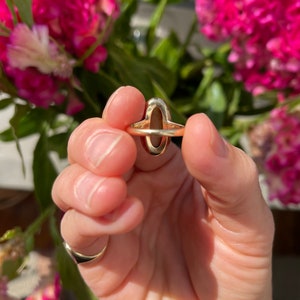 May include: A gold ring with a large oval-shaped gemstone. The gemstone is a deep reddish-brown color.