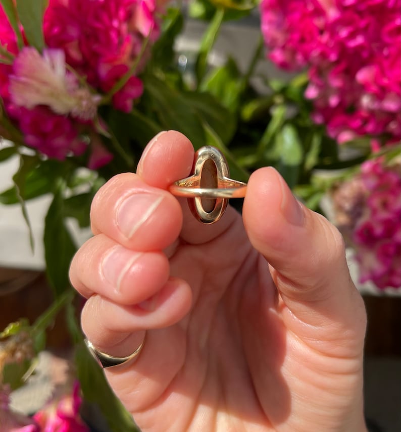 May include: A gold ring with a large oval-shaped gemstone. The gemstone is a deep reddish-brown color.