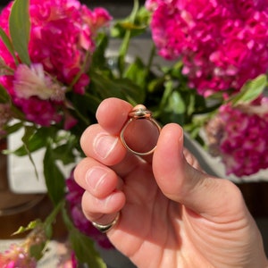 May include: A gold ring with a light pink oval-shaped stone set in a bezel setting.