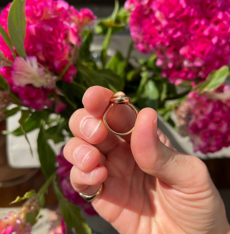 May include: A gold ring with a light pink oval-shaped stone set in a bezel setting.