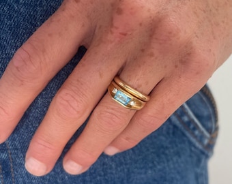 May include: A gold ring with a light blue gemstone and two smaller diamonds. The ring is worn on a finger.