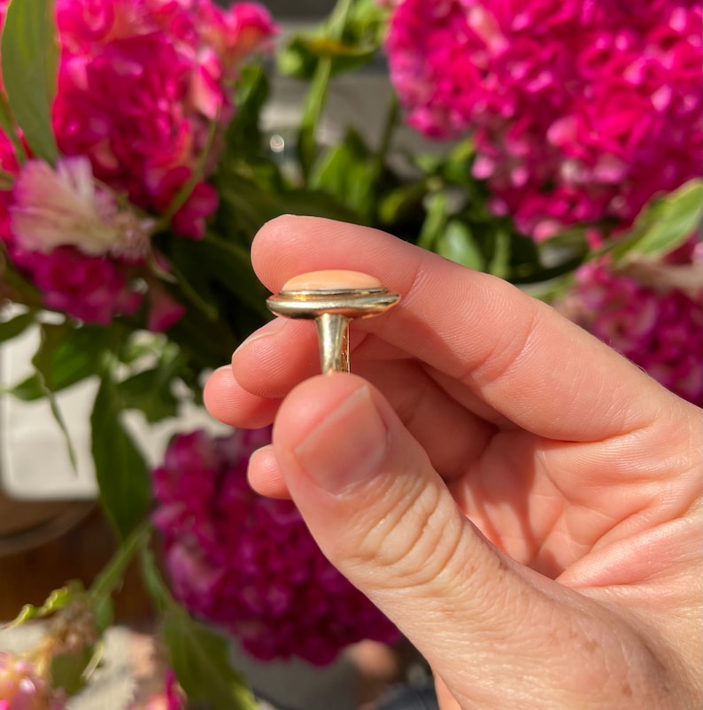 May include: A gold ring with a large oval-shaped pink coral stone set in a bezel setting.