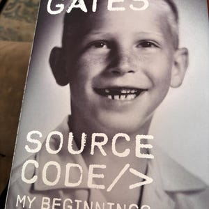 May include: Black and white book cover featuring a young Bill Gates smiling. The title reads '>BILL GATES' at the top, with 'SOURCE CODE/MY BEGINNINGS' below. The image is a vintage photograph of a young boy.