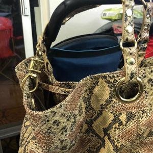 May include: A brown and tan snakeskin handbag with a black leather handle and gold hardware. The bag has a zipper closure and a small pocket on the front.