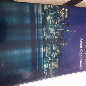 May include: A book titled "Acres of Diamonds" by Russell Conwell. The book cover features a nighttime cityscape with a river and many lit windows. The text on the cover reads "Russell Conwell's Inspiring Book About Opportunity."