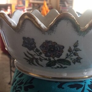May include: White ceramic bowl with a gold rim and floral design. The bowl has a scalloped edge and a base with a gold trim.