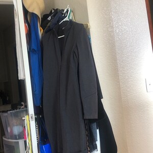 May include: A black long-sleeved dress hanging on a rack in a closet. The dress has a v-neck and a simple design.