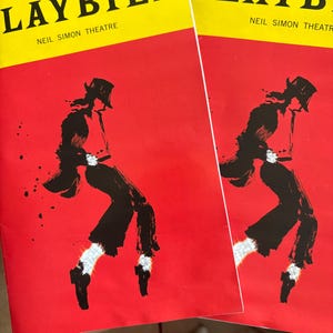 May include: Two red playbill programs with a black and white illustration of a person in a hat and a red background. The text on the playbill reads "Playbill" and "Neil Simon Theatre".
