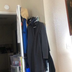 May include: A black long-sleeved dress hanging on a rack with other clothing, including a blue shirt and a white hat.