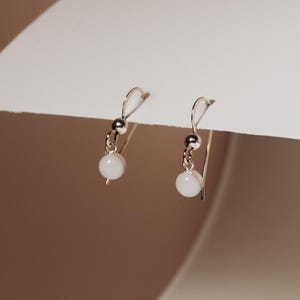 May include: A pair of silver dangle earrings with white round beads.