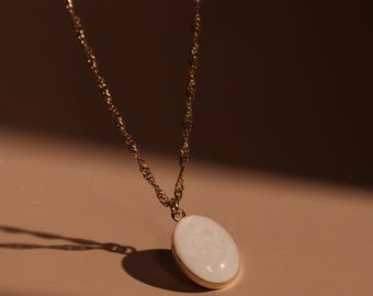 May include: A gold chain necklace with a white oval pendant. The pendant has a textured surface.