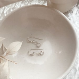 May include: A pair of silver earrings with small round white stones hanging from a silver hook.