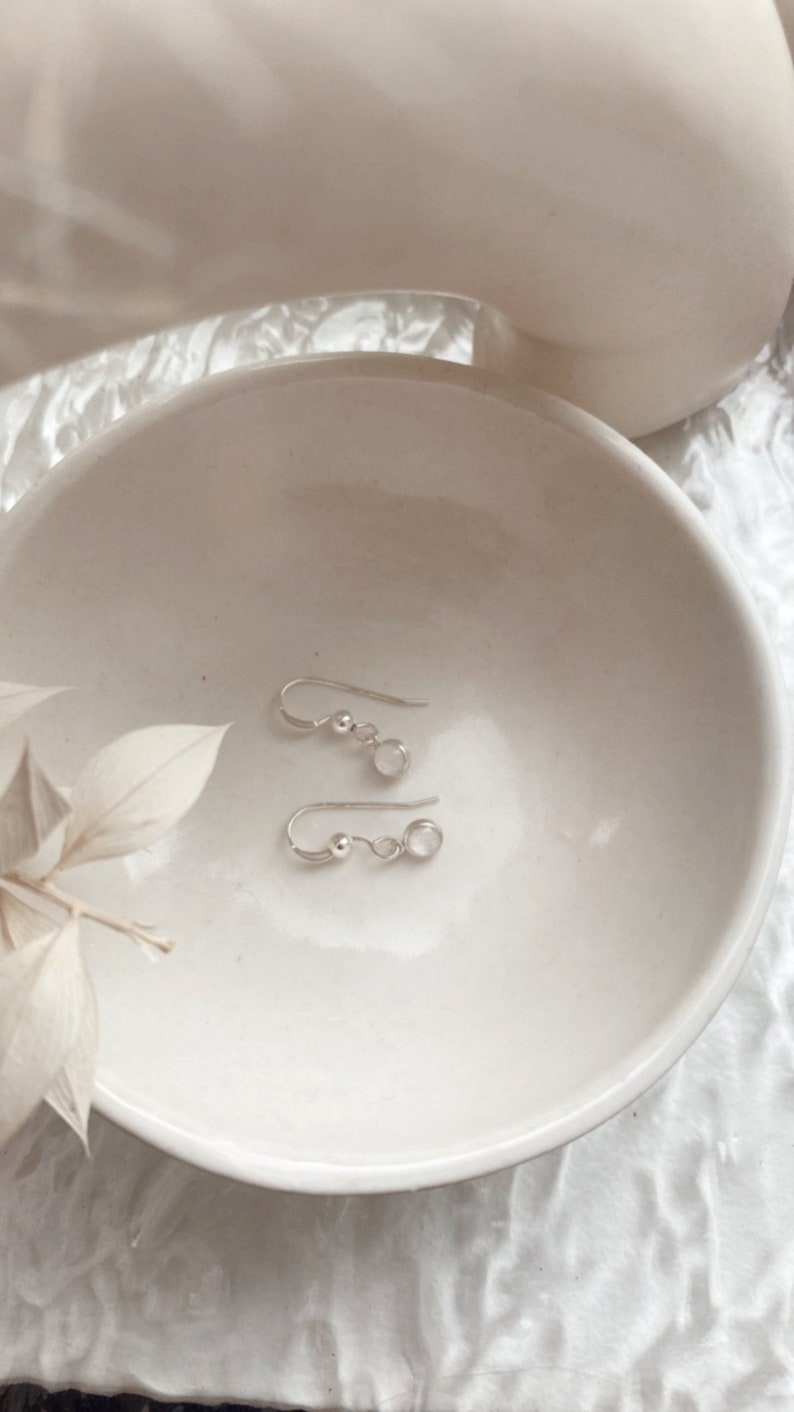 May include: A pair of silver earrings with small round white stones hanging from a silver hook.