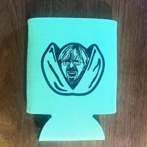 May include: A light teal can cooler featuring a black graphic of a man's face with glasses and a beard. The cooler is made of a textured material and has a cutout at the bottom.