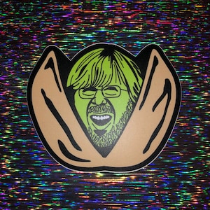 May include: A green and brown sticker of a person's face with a wide open mouth and a beard, inside of a brown peanut shell.