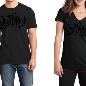 May include: Black crew neck t-shirt with the text "Justified" in a stylized font. The image shows the t-shirt on a person. The t-shirt is made of a soft material. The image also shows a black v-neck t-shirt with the same text.