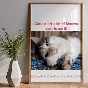May include: A framed print featuring a cat with white and gray fur, resting on a blue patterned surface. The text "Cats: A little bit of heaven sent to earth" is displayed above the cat. The bottom border has paw prints and hearts.