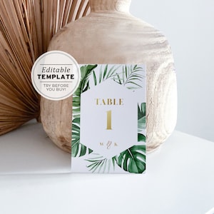 May include: A white card with a gold hexagonal frame featuring the text "TABLE 1" and the initials "W & K". The card is surrounded by a green tropical leaf border.