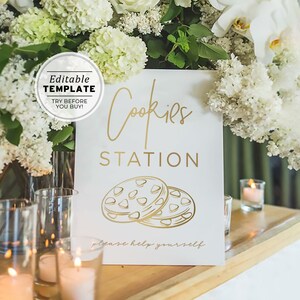 Puede incluir: Un cartel blanco con letras doradas que dice "Cookies Station" y "Por favor, sírvete". El cartel presenta un gráfico de dos galletas con chispas de chocolate. El cartel está sobre una mesa de madera con velas y flores en el fondo.