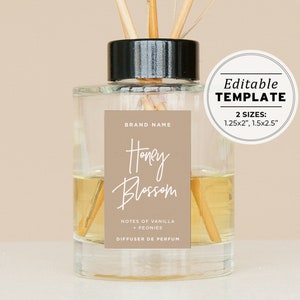 Puede incluir: Una botella de difusor de vidrio transparente con tapa negra y palitos de madera. La etiqueta es marrón con texto blanco que dice "BRAND NAME", "Honey Blossom", "NOTES OF VANILLA + PEONIES", y "DIFFUSER DE PERFUM". La etiqueta también incluye una plantilla editable en dos tamaños: 1,25x2 pulgadas y 1,5x2,5 pulgadas.