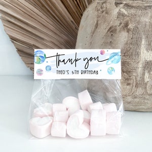 May include: A clear plastic bag filled with pink heart-shaped marshmallows. A thank you tag with a space theme is attached to the bag. The tag says "Thank you" and "Theo's 5th Birthday".