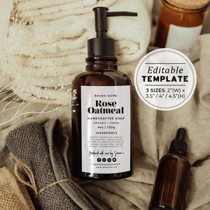 May include: A brown glass bottle with a black pump dispenser filled with liquid soap. The label reads "Rose Oatmeal Handcrafted Soap Organic Vegan 4oz | 120g Ingredients: Organic Coconut Oil, Organic Sunflower Oil, Organic Sweet Almond Oil, Organic Avocado Oil, Organic Coconut Milk, Water, Organic Lavender Essential Oil Handmade with love by Joom - BRANDNAMEMAKABLE www.website.com". The bottle is sitting on a beige fabric surface with a brown towel and a small brown glass bottle with a dropper.